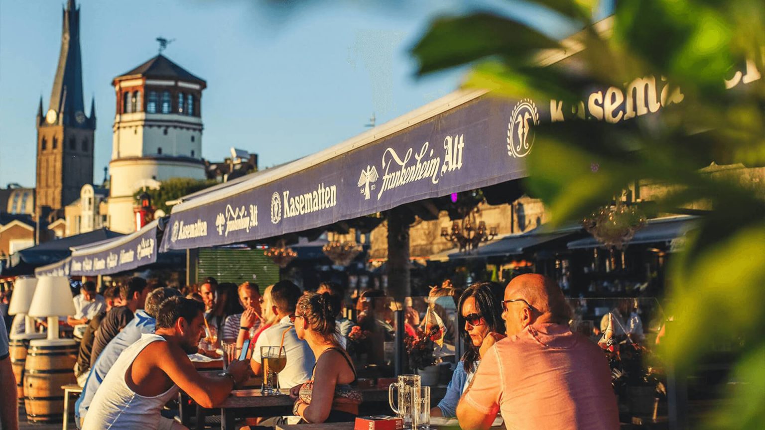 Besucher genießen an einem sonnigen Tag am Rheinufer in den Kasematten der Location Frankenheim ihre Getränke in vollen Zügen.