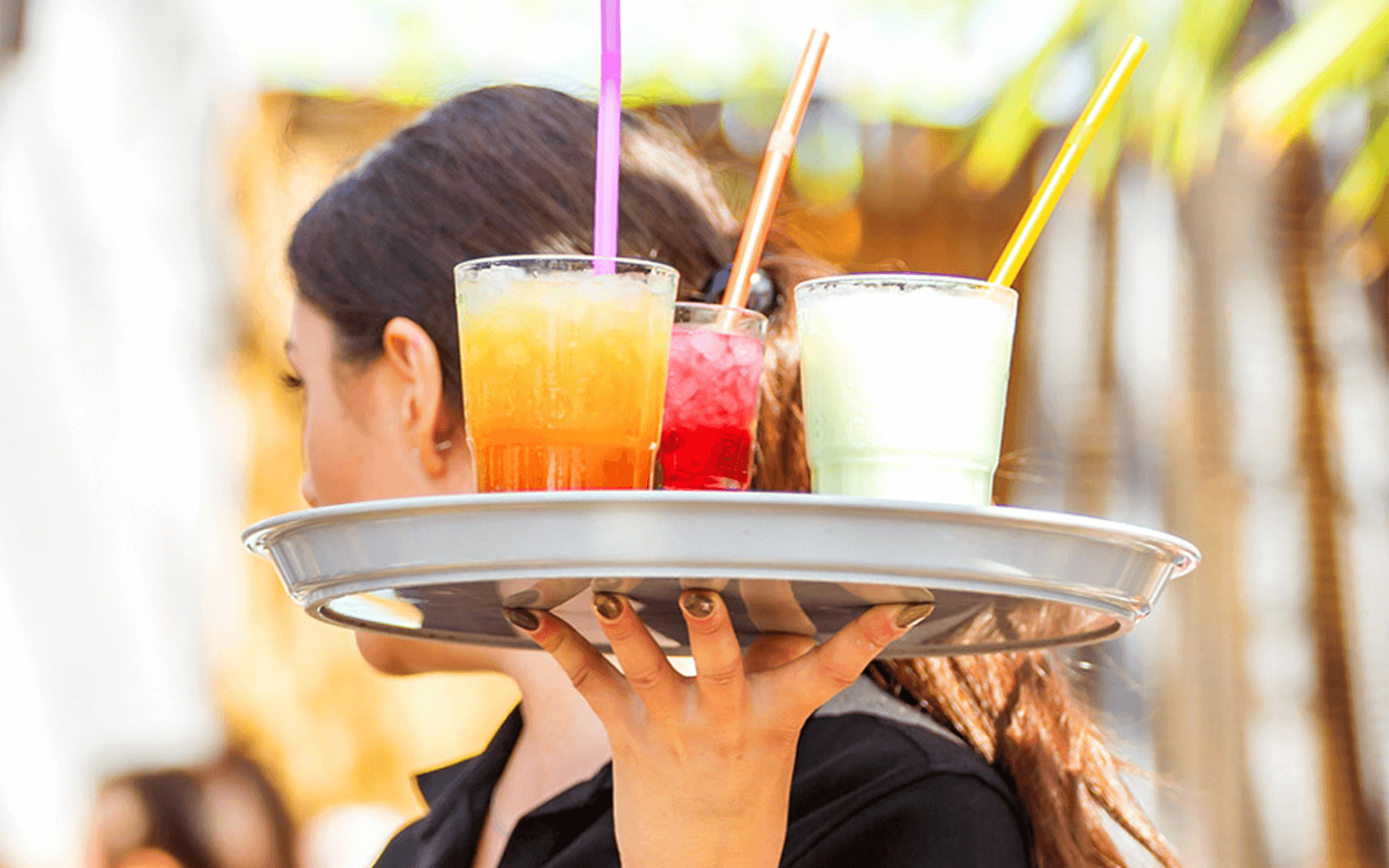 Eine Kellnerin balanciert Getränke auf einem Tablett mit drei Cocktails.